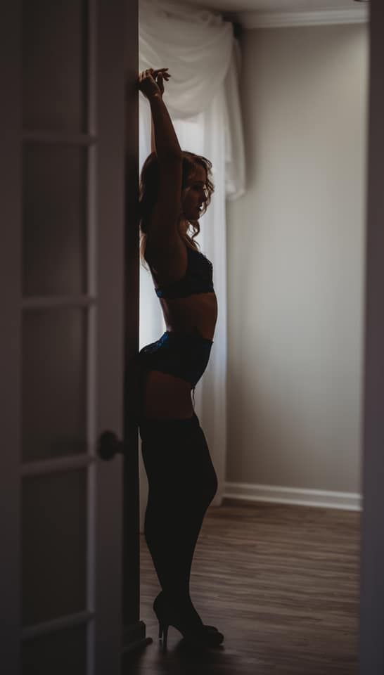 Dramatic silhouette of person stretching in lingerie against light through doorway.