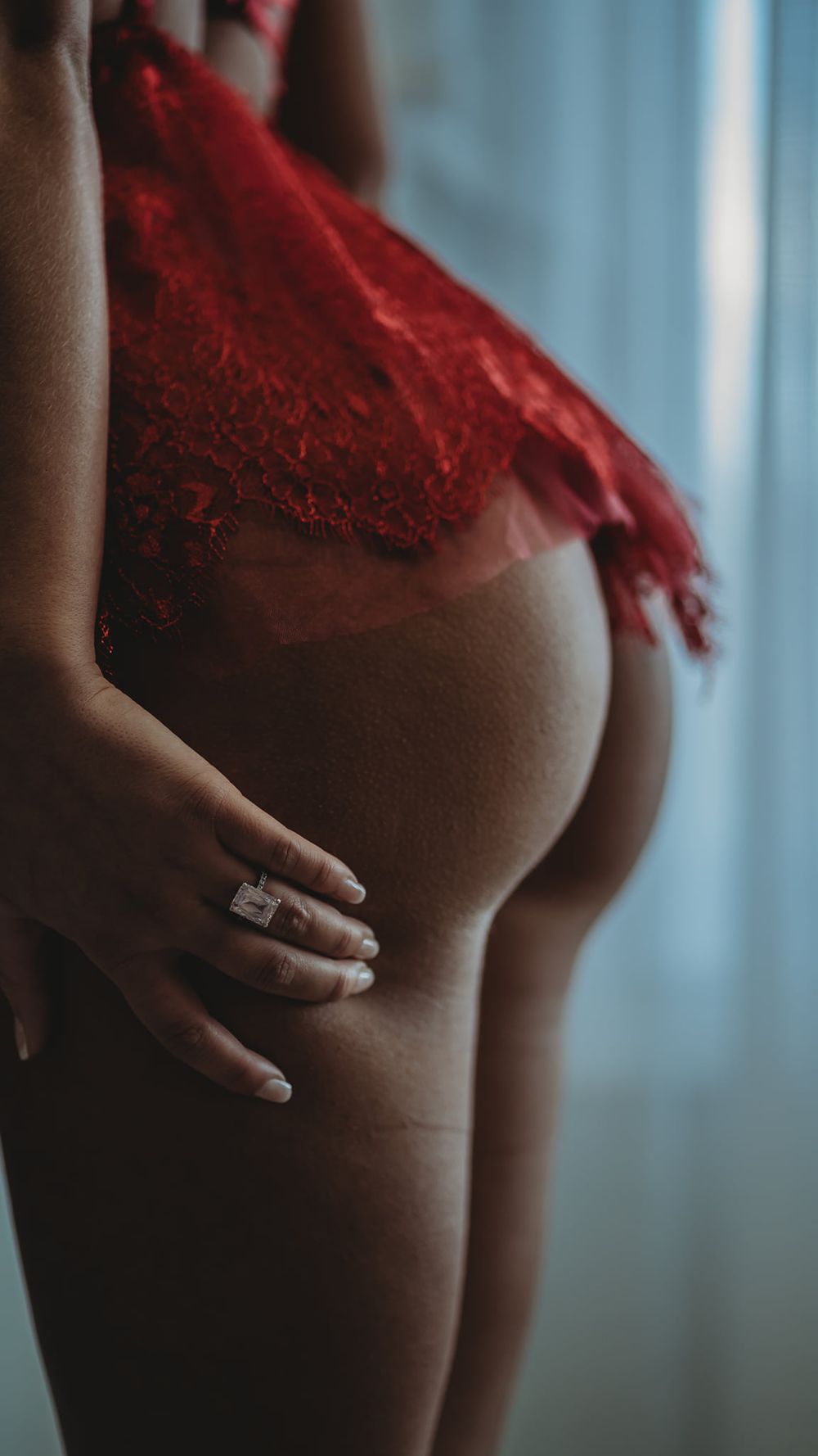 Side view of figure in flowing red lace garment showing engagement ring.