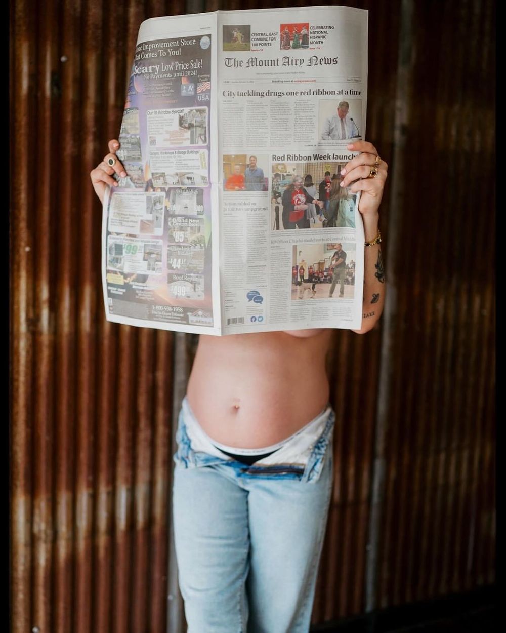 Person holding up newspaper in front of themselves wearing light blue jeans.