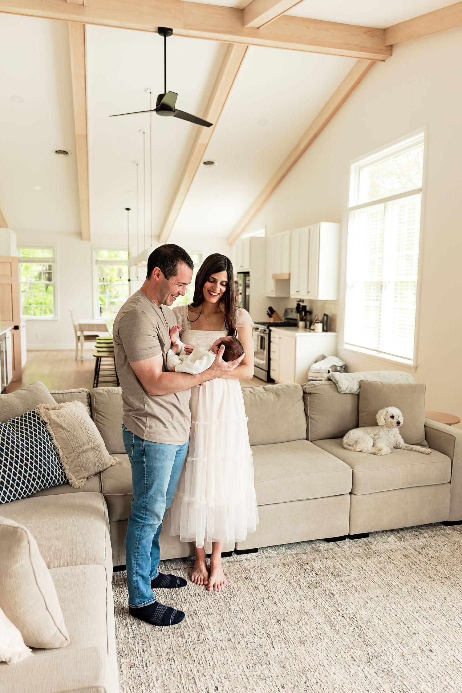 Tender moment between parents and newborn baby in casual home setting by window.