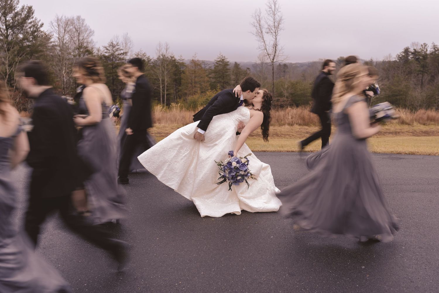Wedding party walking fast past the newlyweds for a creative portrait at Lunas Trail Farm in Westfield, NC