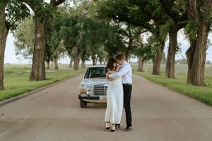 A romantic moment captured on a tree-lined avenue with a classic Mercedes-Benz in the background.