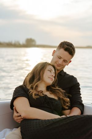 Couple cuddling on boat during golden hour with serene water backdrop.