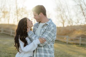 A couple embraces in a romantic outdoor setting during golden hour with autumn trees in the background.
