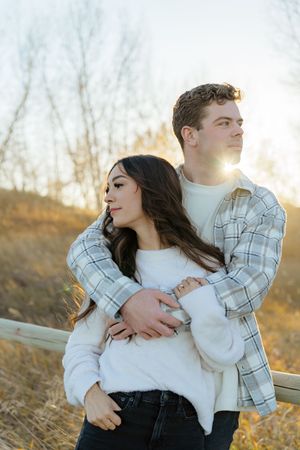 A couple embraces in a romantic outdoor setting during golden hour with sunlight glowing behind them.