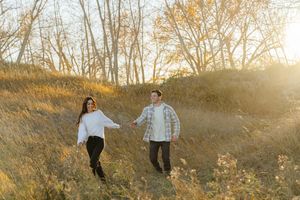 A couple stands together in a golden field during sunset creating romantic silhouettes against the warm sky.