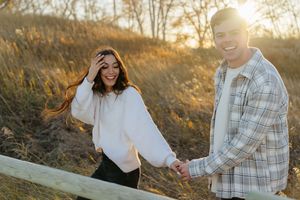 Couple sits together outdoors during golden hour sunset in a grassy field with autumn lighting and plaid shirt details.