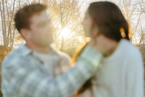 A couple shares an intimate moment during a golden sunset in a wooded outdoor setting.