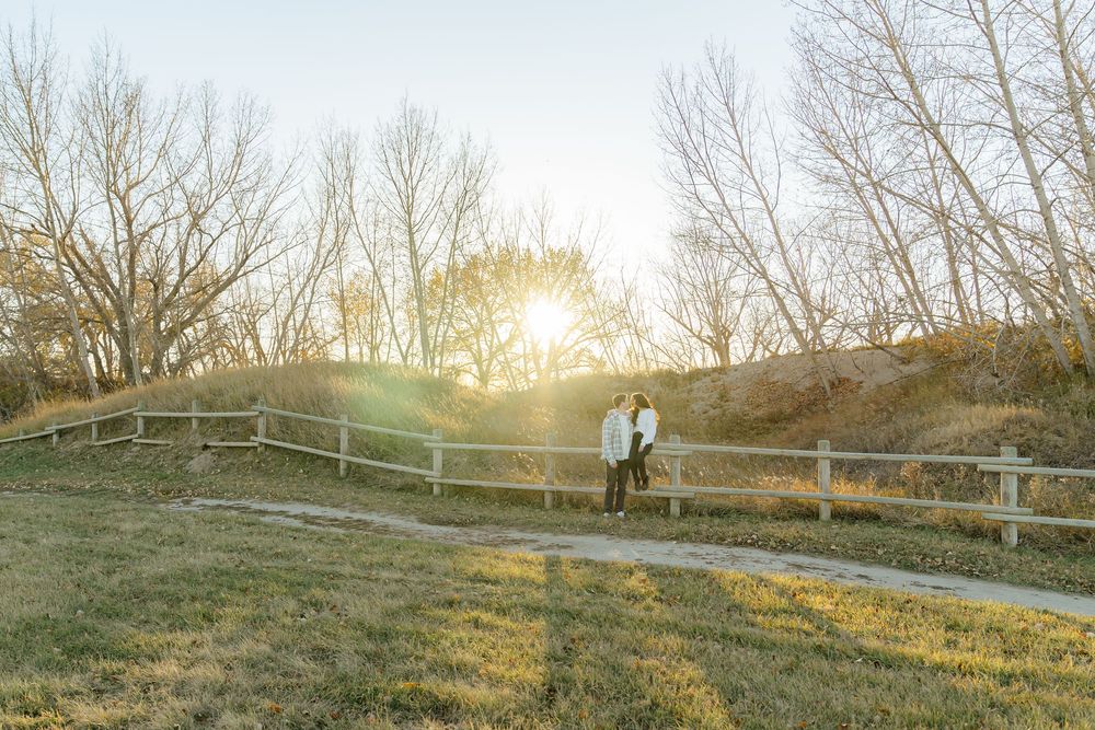 A serene panoramic view of a rural landscape at sunset with bare trees and wooden fences along a grassy hillside.