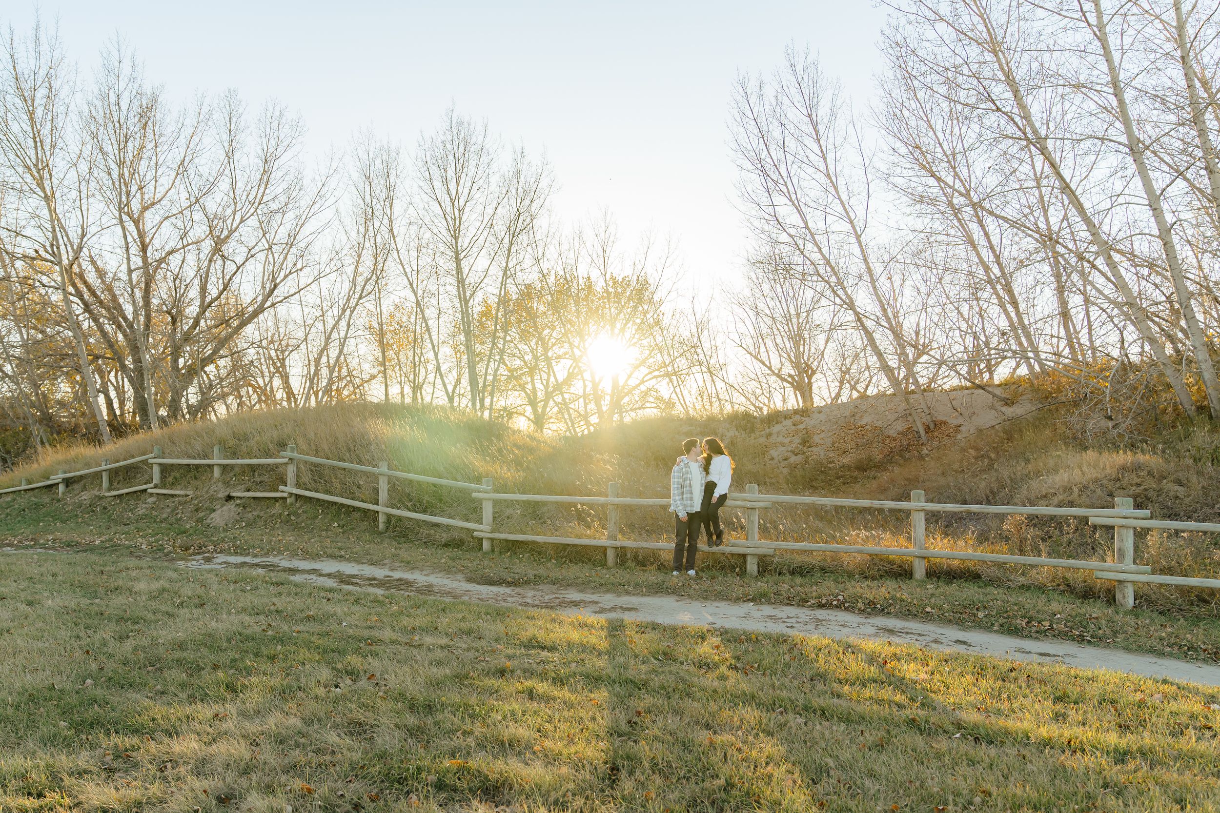 A serene panoramic view of a rural landscape at sunset with bare trees and wooden fences along a grassy hillside.