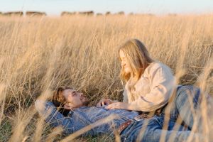 A couple lying in a golden wheat field during sunset sharing an intimate moment.