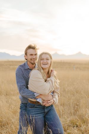 Couple embracing and laughing together in a sunlit field of golden grass.