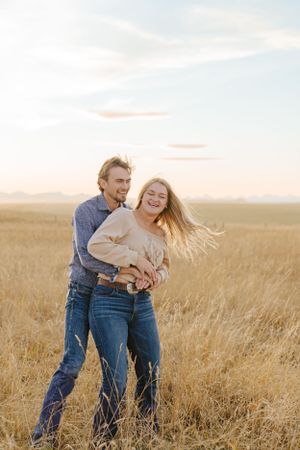 Happy couple sharing a joyful moment in a wheat field at sunset.