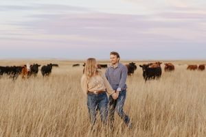 Two people walking through a field with cattle grazing in the distance at dusk.