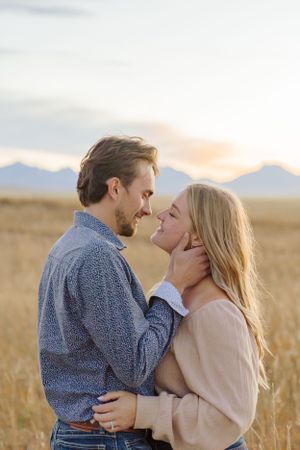 Intimate moment between a couple in a golden wheat field with mountains in the background.
