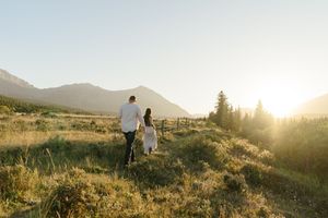 Couple walking on scenic mountain trail during golden hour sunset with warm backlit glow in nature.