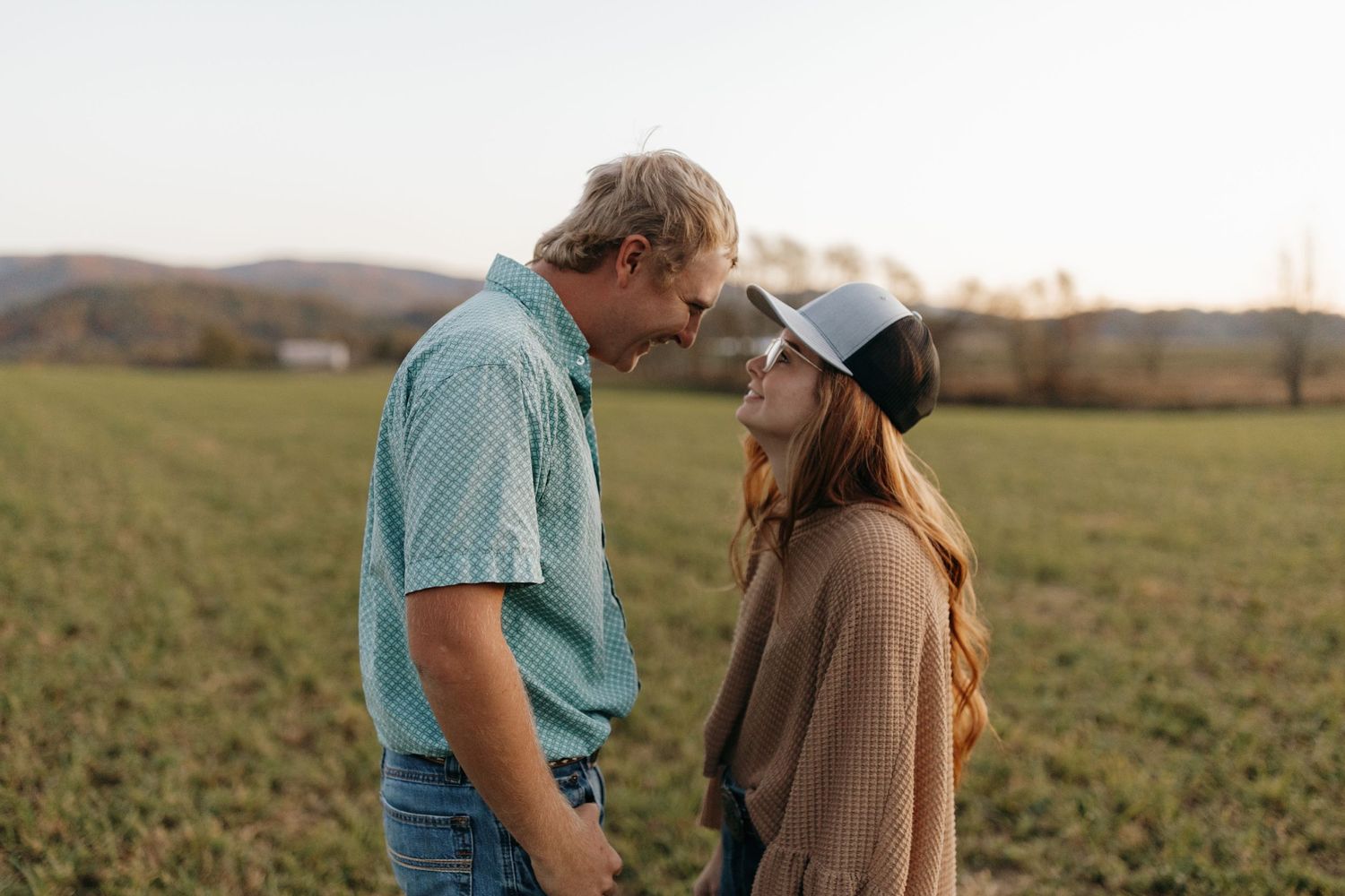A couple gazes at each other while standing in a field during golden hour.
