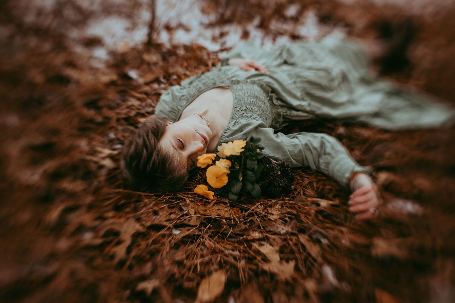 Person lying on autumn leaves in a forest setting with moody golden light filtering through the trees. Journey session. Whitney Popp