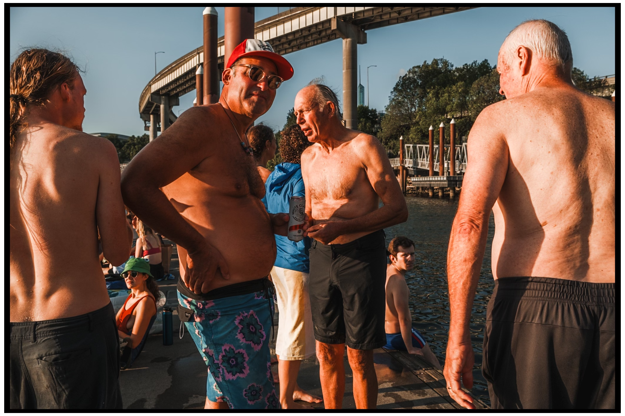 Group of shirtless swimmers gathered at waterfront during sunset. Willamette River, Portland, OR