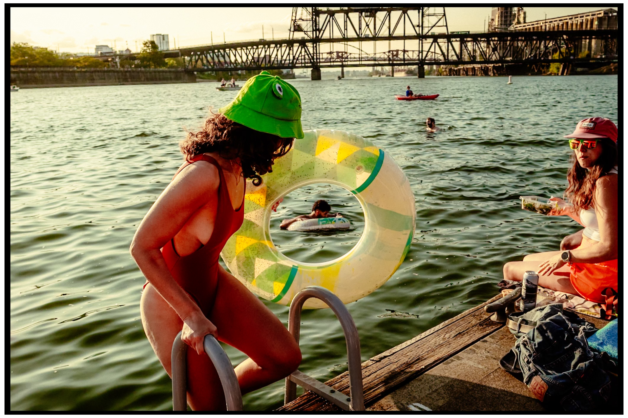 Person with green hat and inflatable float enjoys summer swimming beneath bridge. Willamette River, Portland, OR