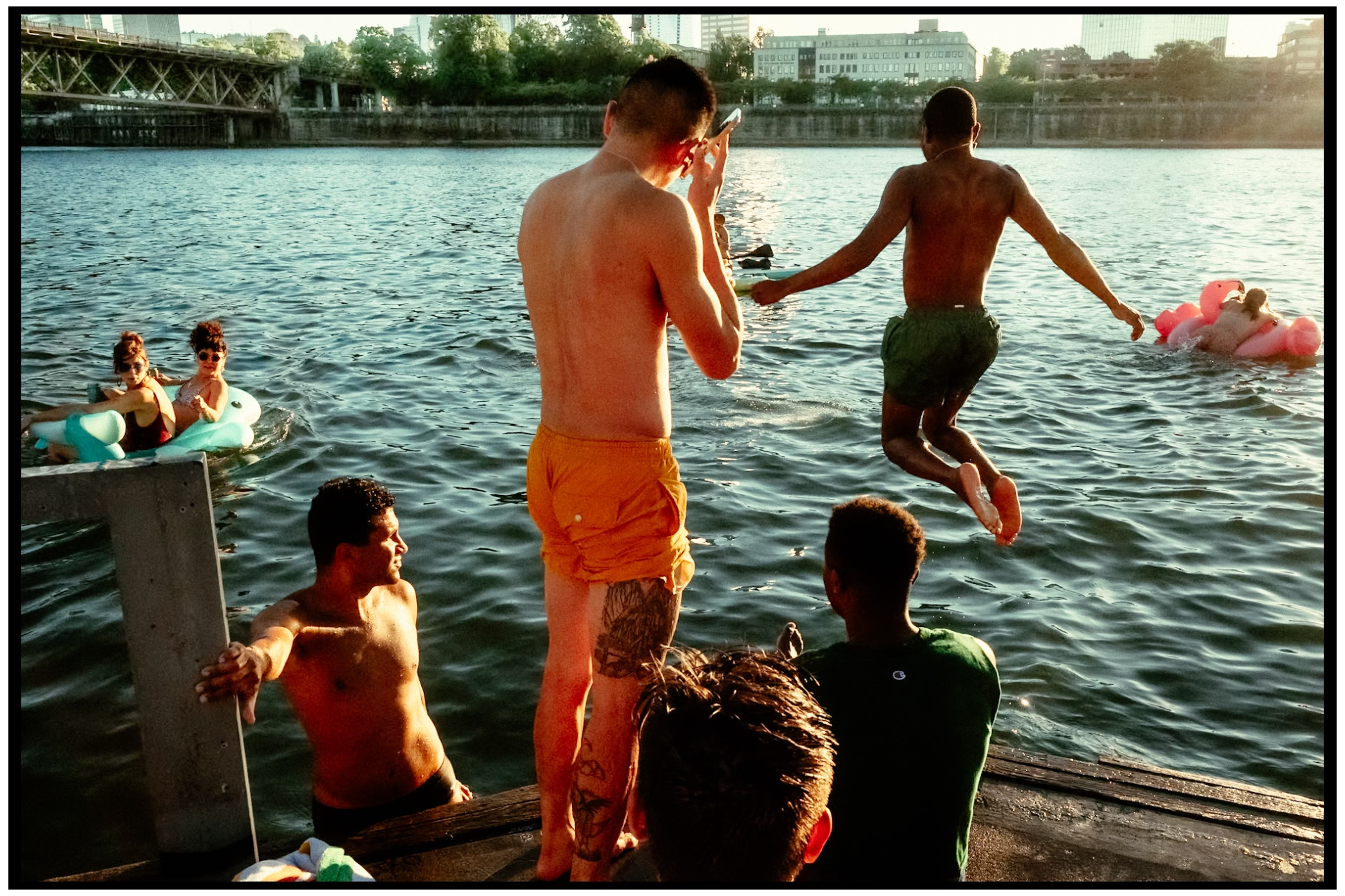 Group enjoying summer activities by a lake with swimmers and floats. Willamette River, Portland, OR
