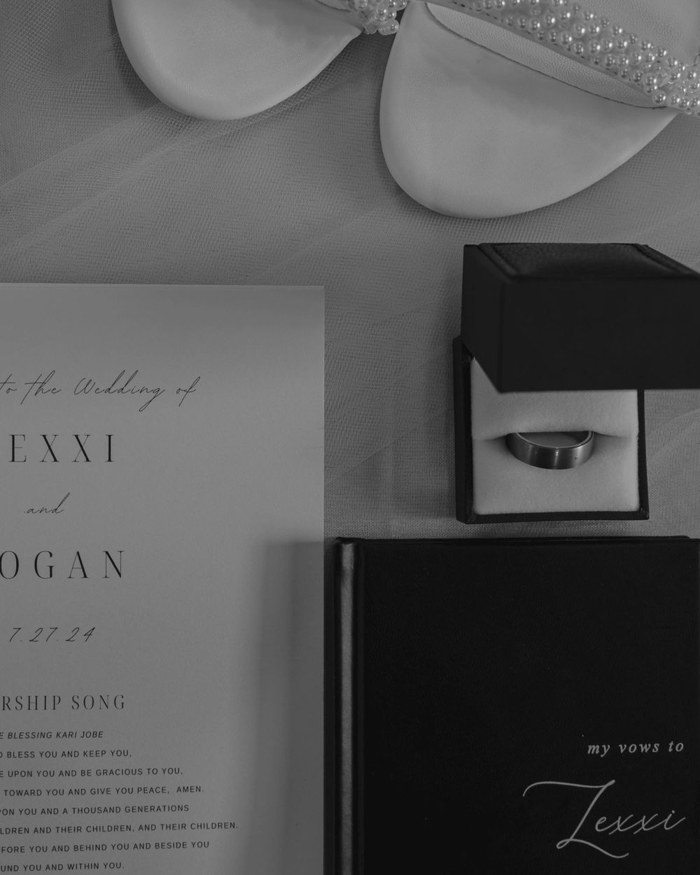 Monochrome wedding details including ring box and invitation with cursive text.