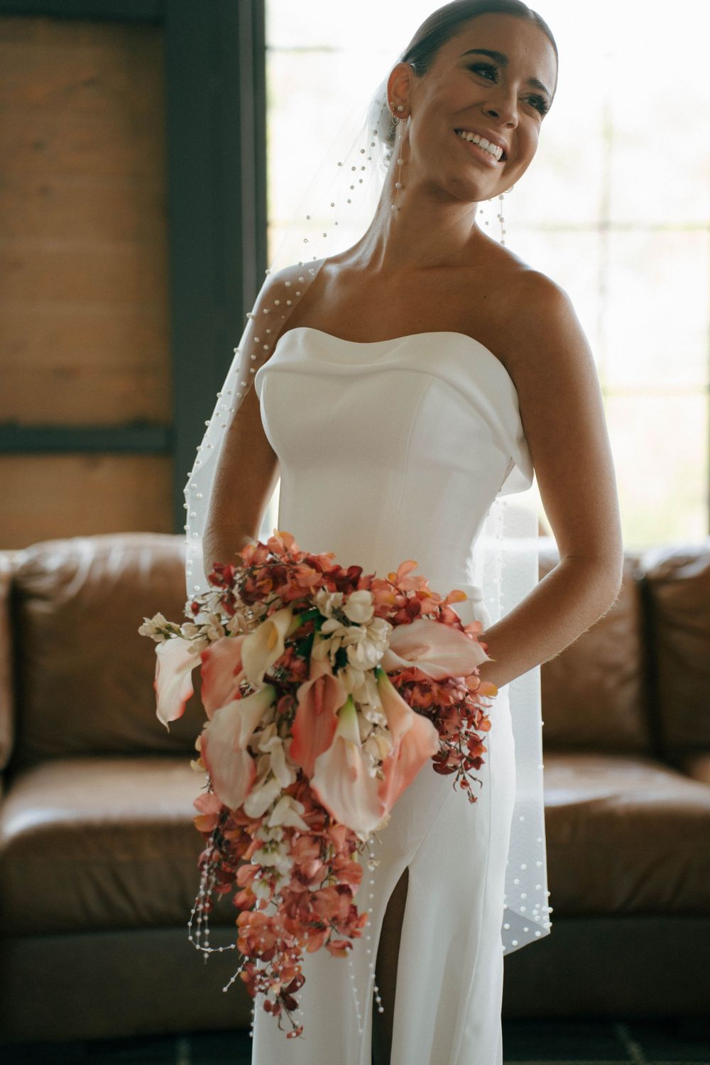 Radiant bride in strapless gown holding cascading coral and white floral bouquet.