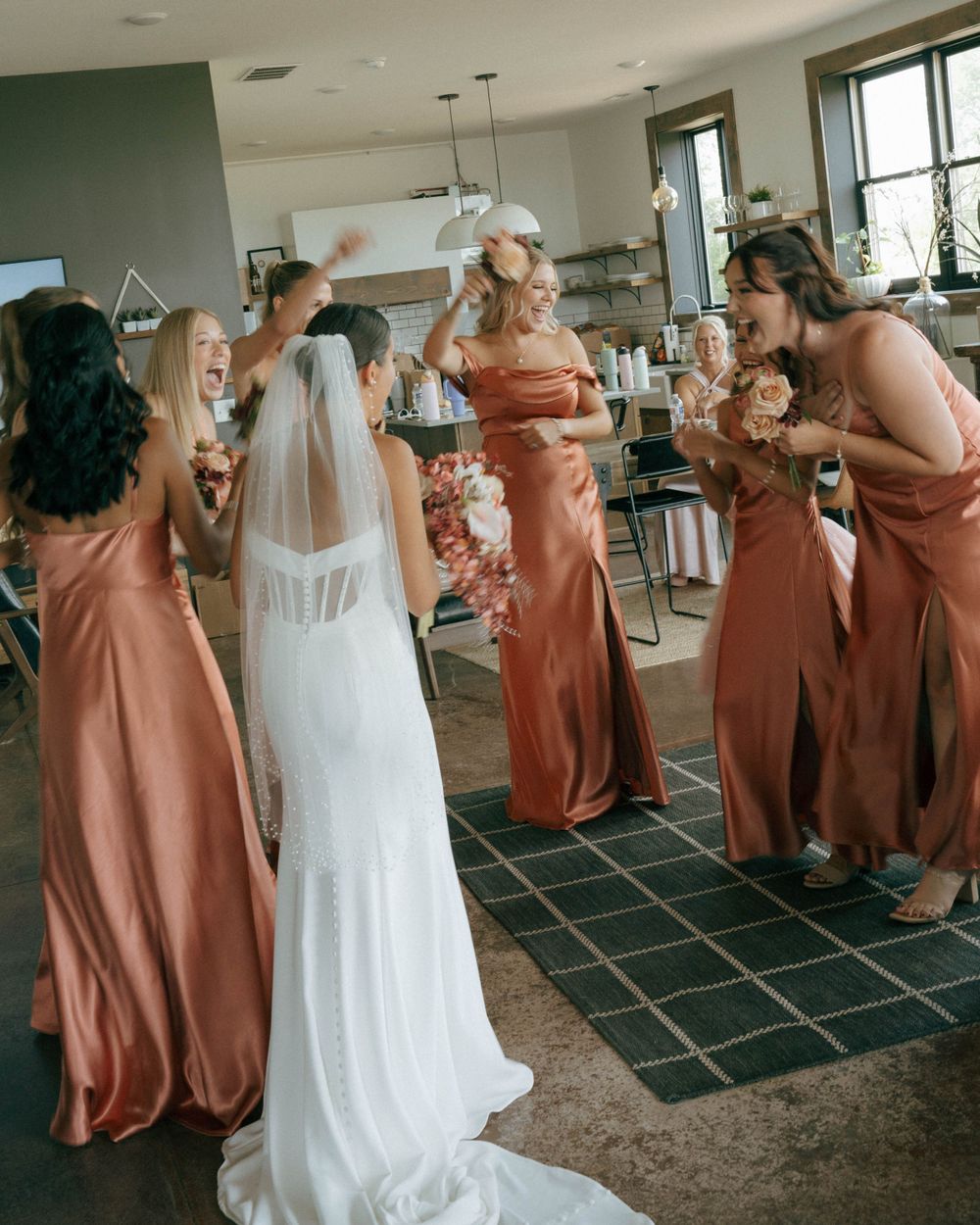 Bridesmaids in coral dresses gather around bride in white gown during wedding preparations.