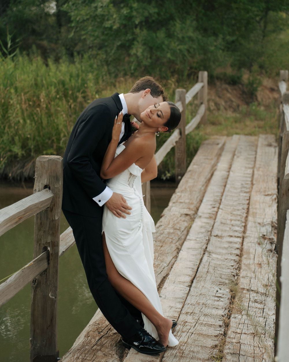 Romantic couple poses on wooden bridge during wedding photoshoot.