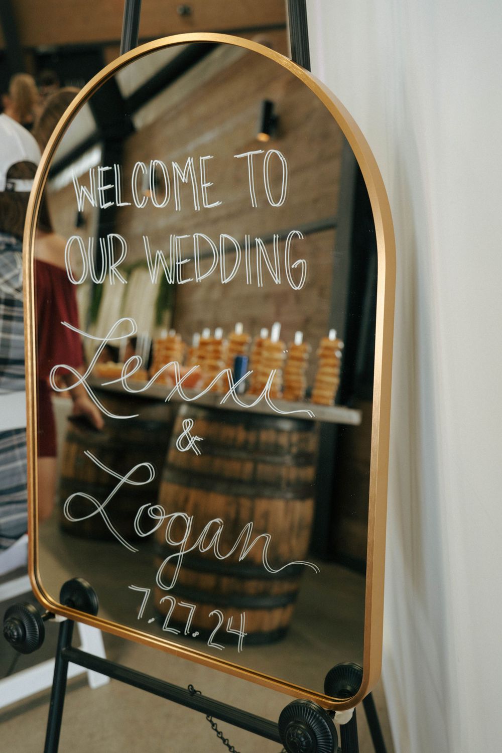 Elegant gold-framed wedding welcome sign for Lexi and Logan's celebration with handwritten text on mirror surface.