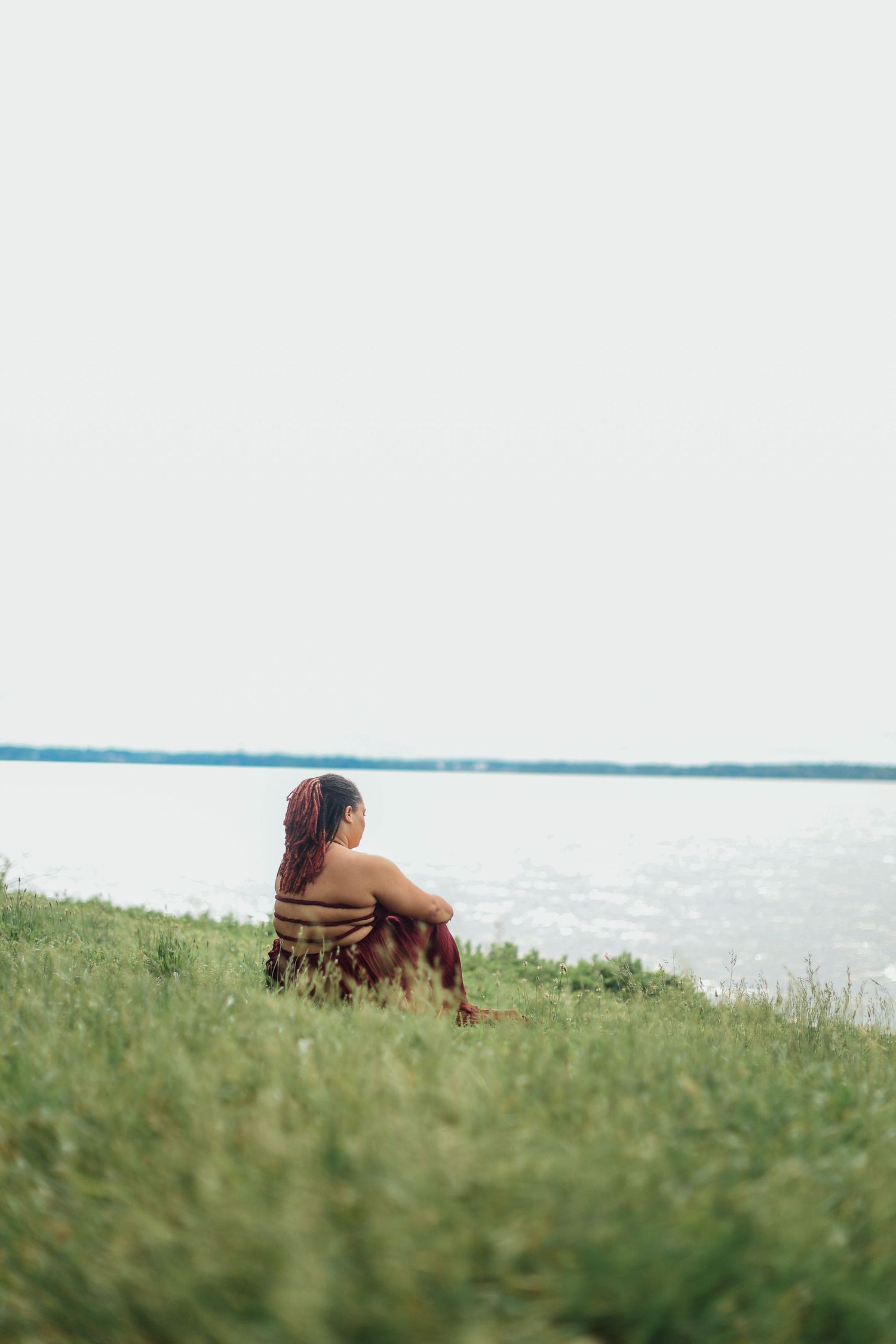 Someone lying down on green grass near a lake or waterfront on a sunny day, enjoying the peaceful scenery.