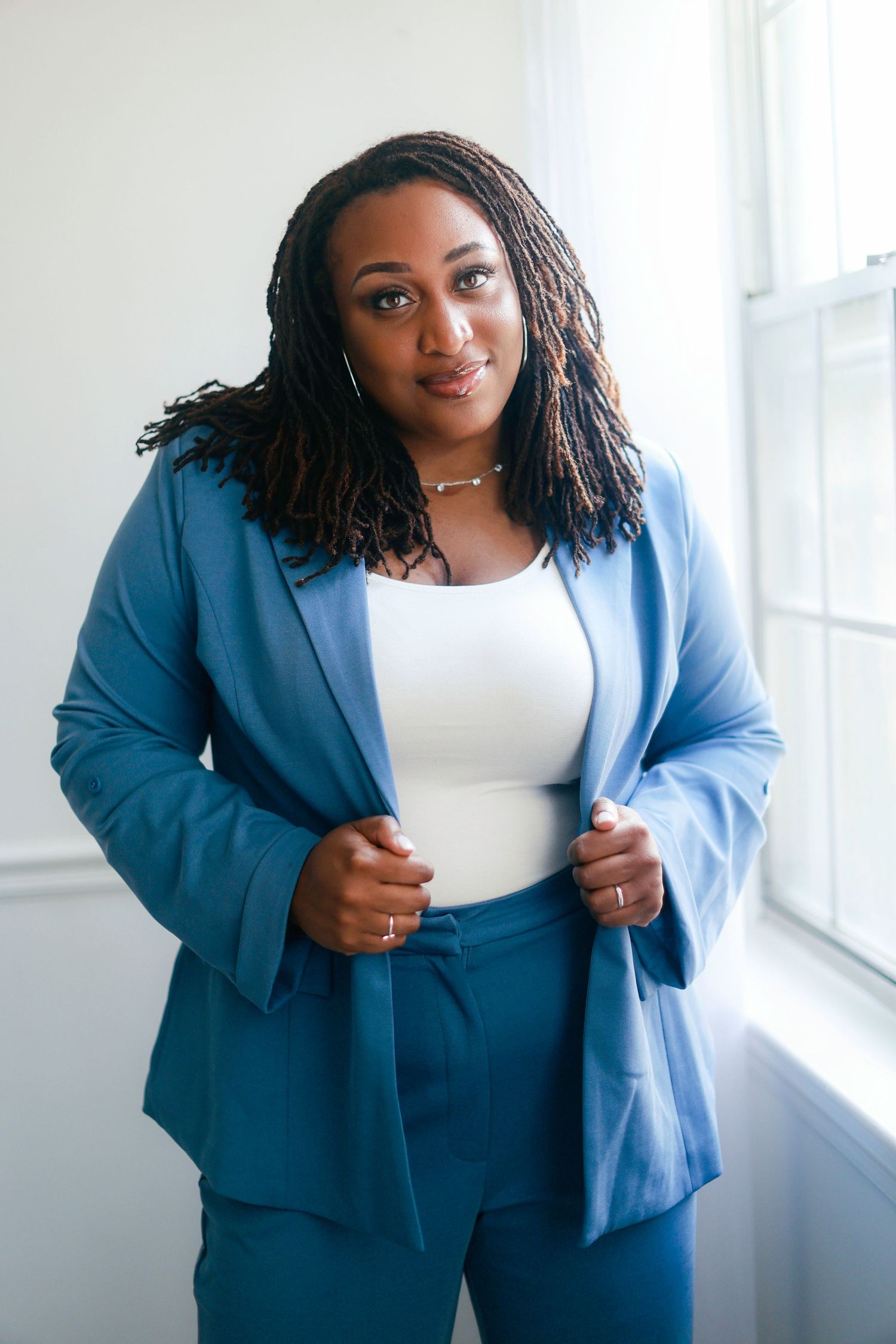 A professional in a bright blue blazer and white top poses confidently in a bright office setting.