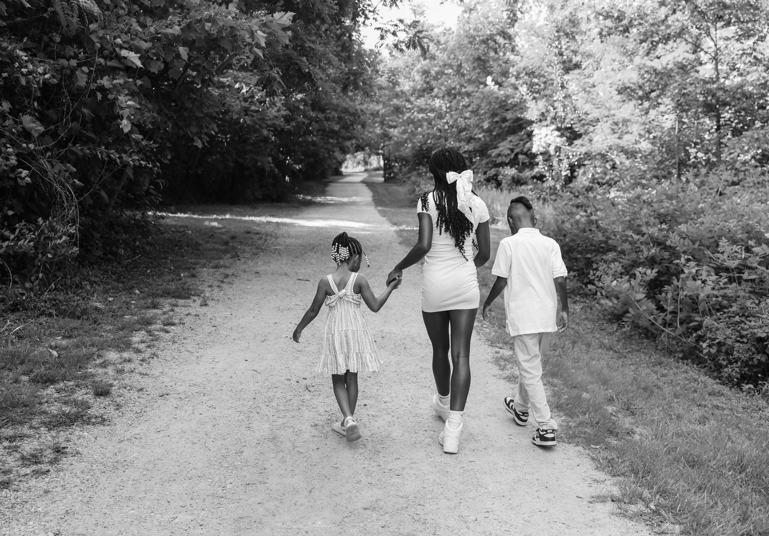 Three people walking together down a scenic tree-lined dirt path on a sunny day.