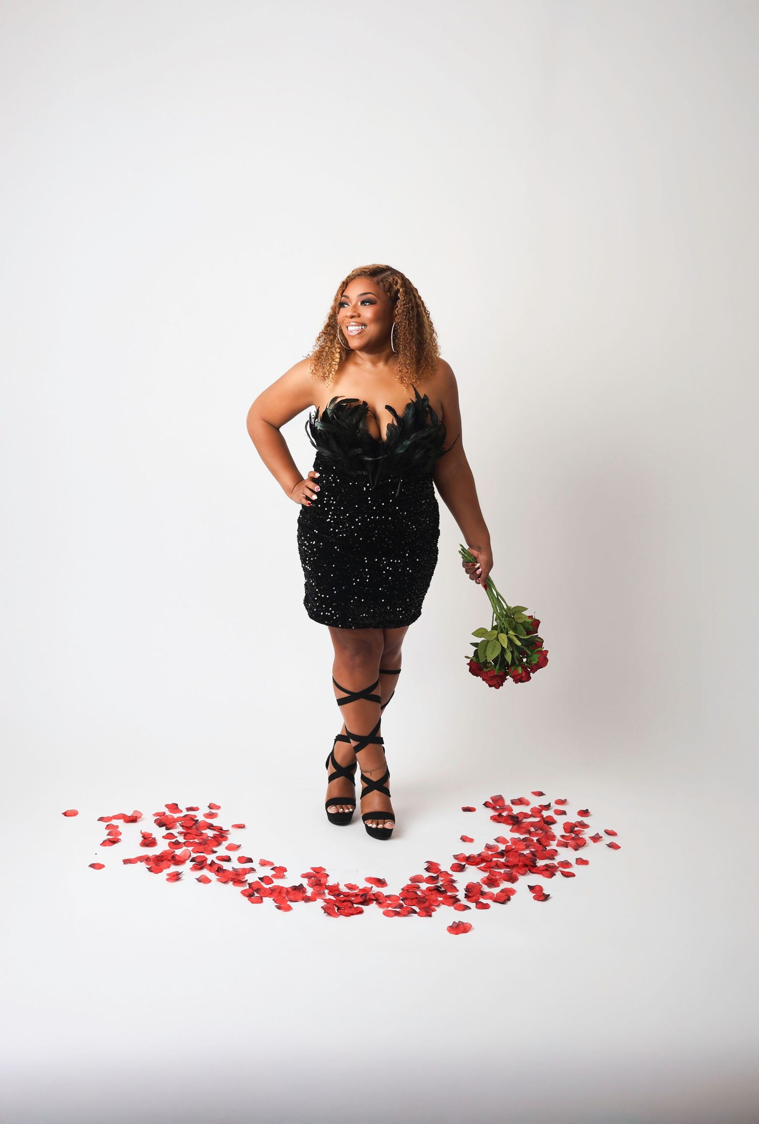 A figure in a black dress drops red rose petals across a white studio floor in a three-part sequential photo series.