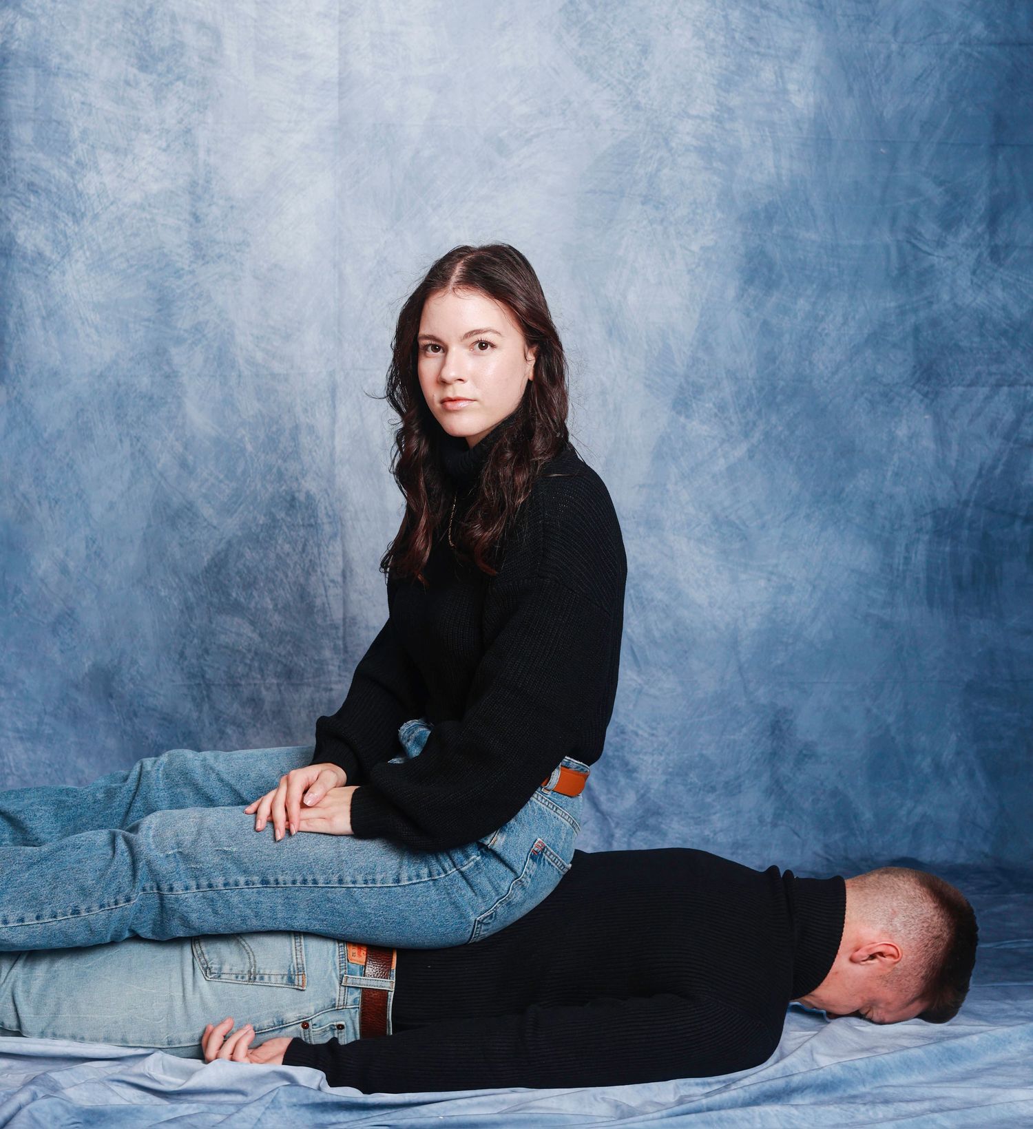 A person in black attire reclines on a light blue backdrop in a series of artistic portrait poses.