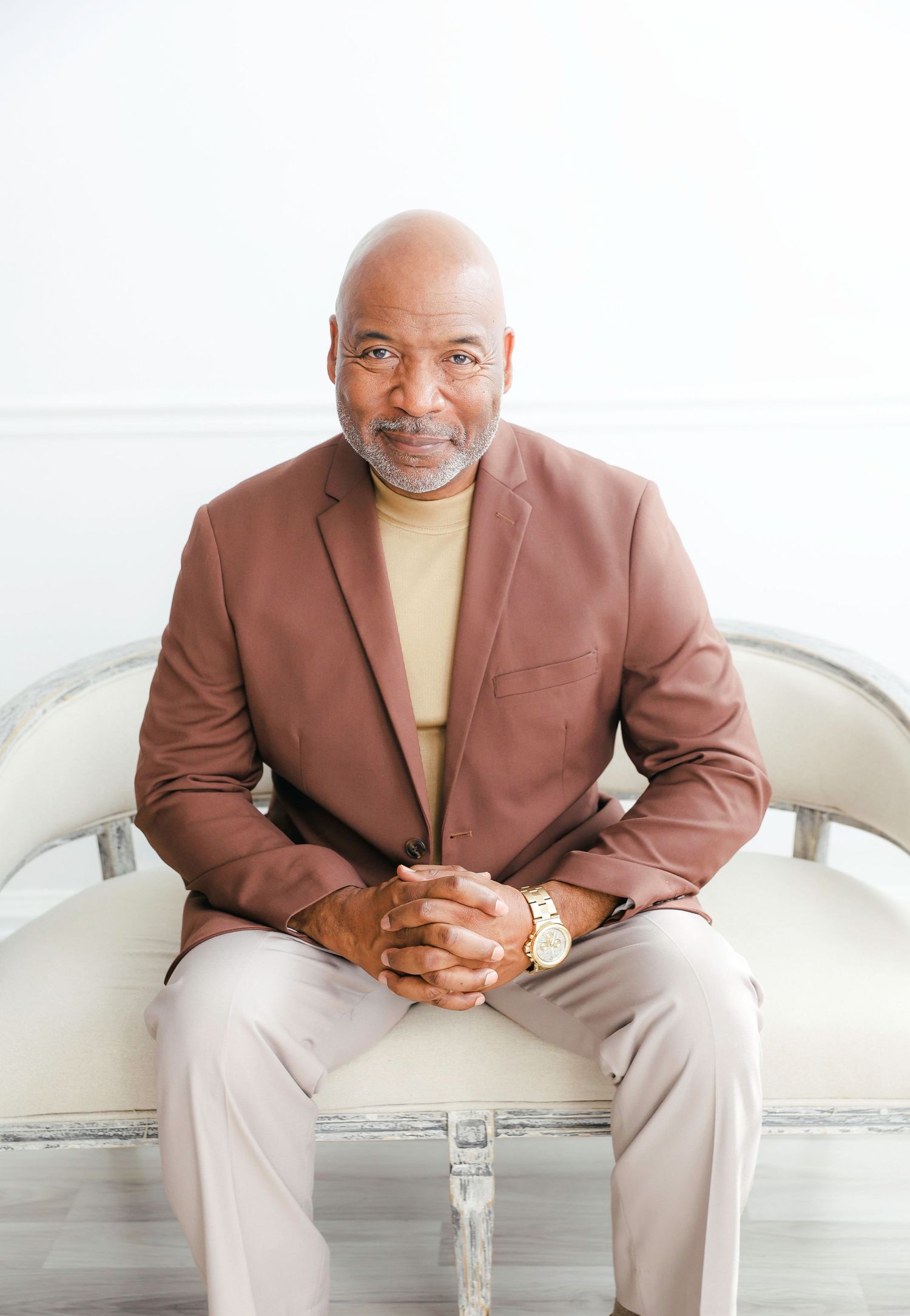 A person wearing a brown blazer and beige sweater sits on a white couch in a modern interior setting.