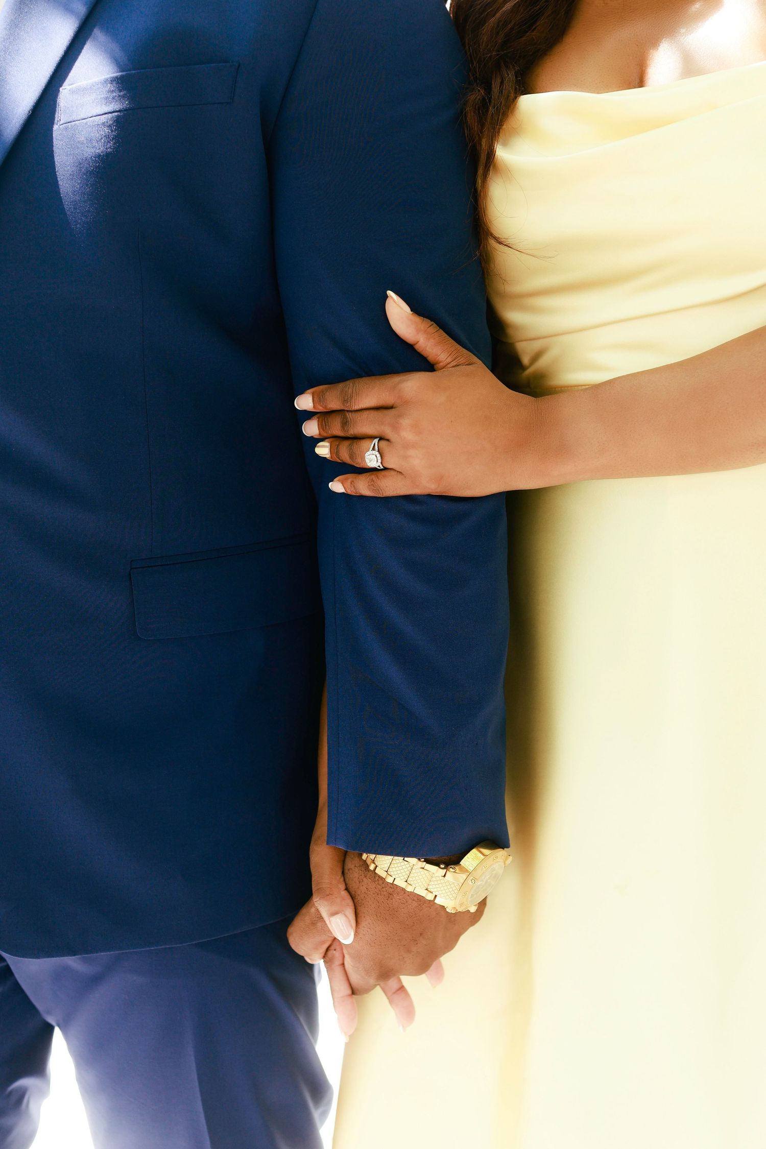 Close-up of a couple in formal attire embracing, showing navy suit jacket and pale yellow dress details.