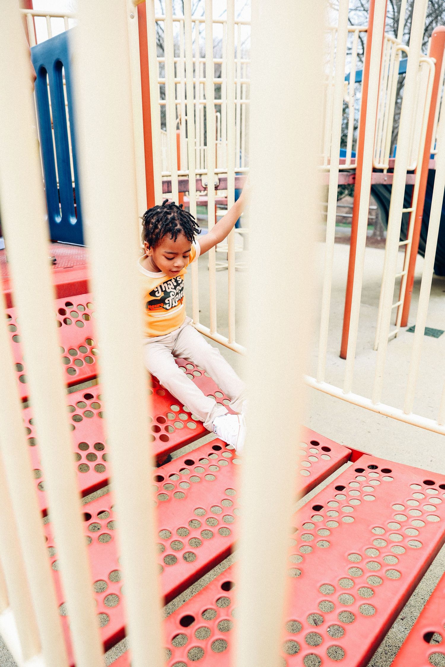 Small child in yellow shirt plays on pink playground equipment behind vertical bars.