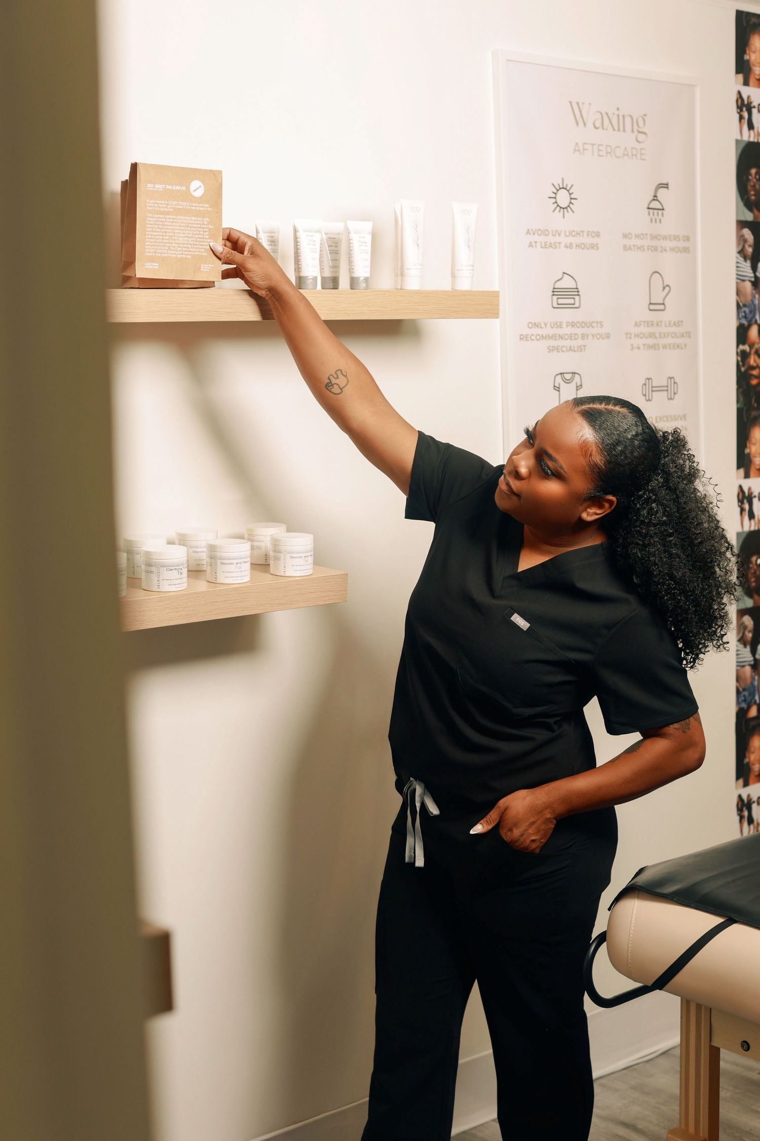Healthcare professional in black scrubs reaching for products on wooden shelving in a medical spa or wellness setting.