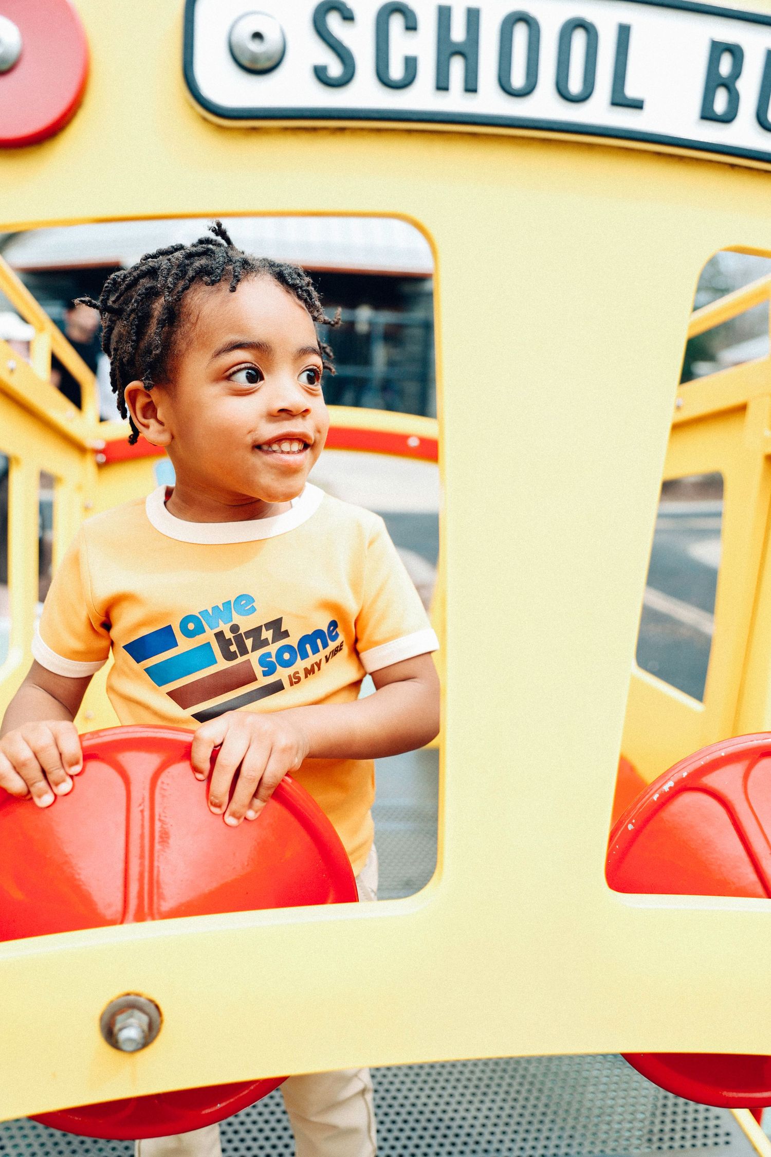 Child peeks out window of yellow school bus with bright smile while wearing striped shirt.