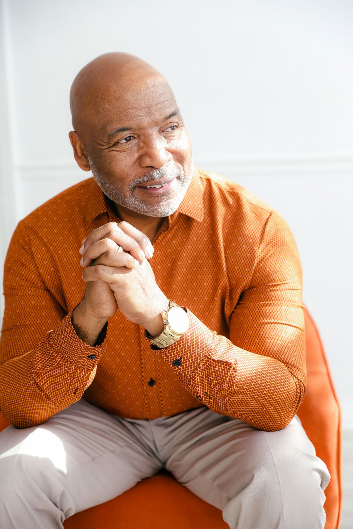 A person in a bright orange sweater sits thoughtfully against a white background in a series of candid poses.