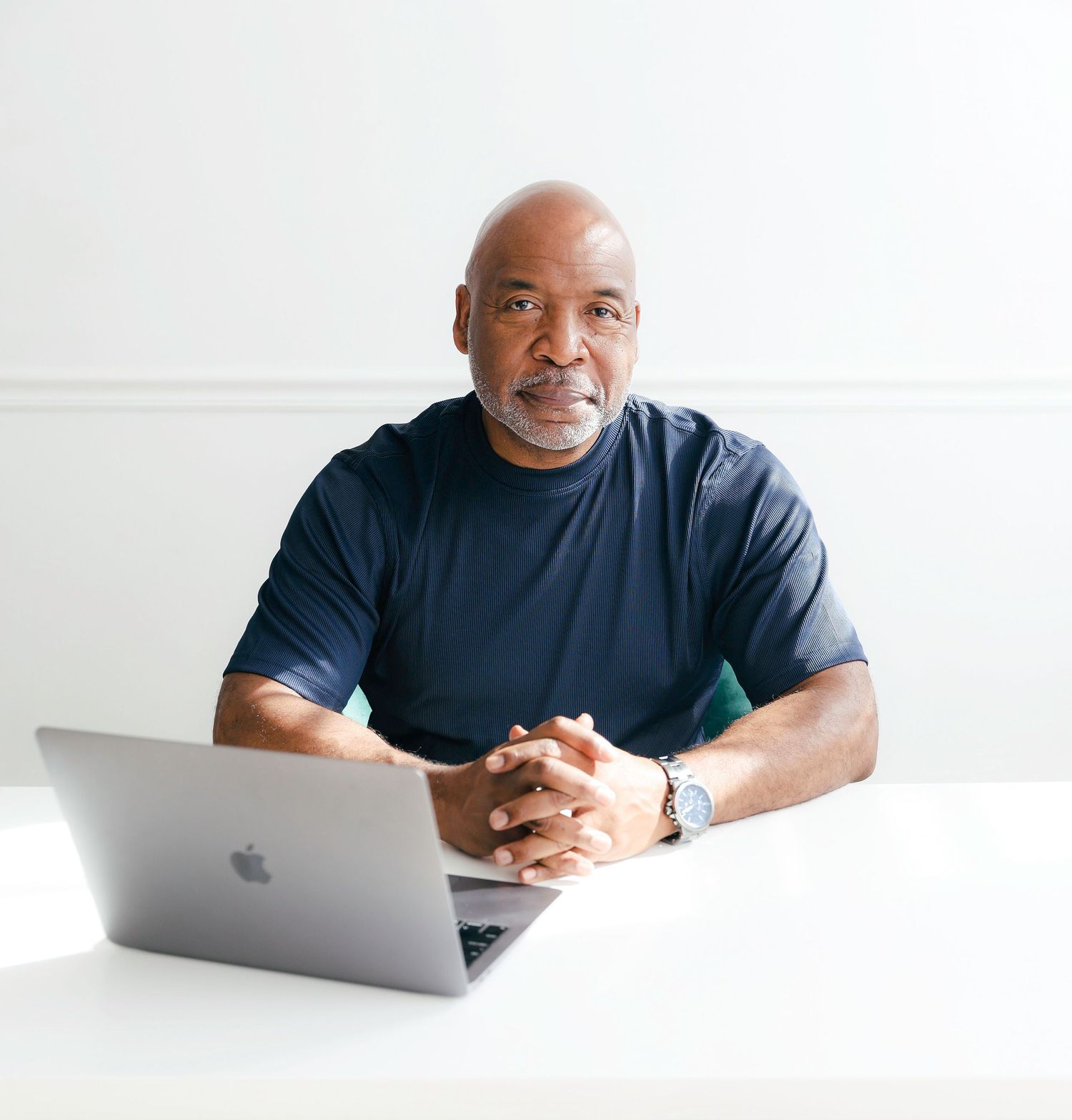Person in a navy shirt sits at a white desk with a laptop, photographed from multiple angles in a bright setting.