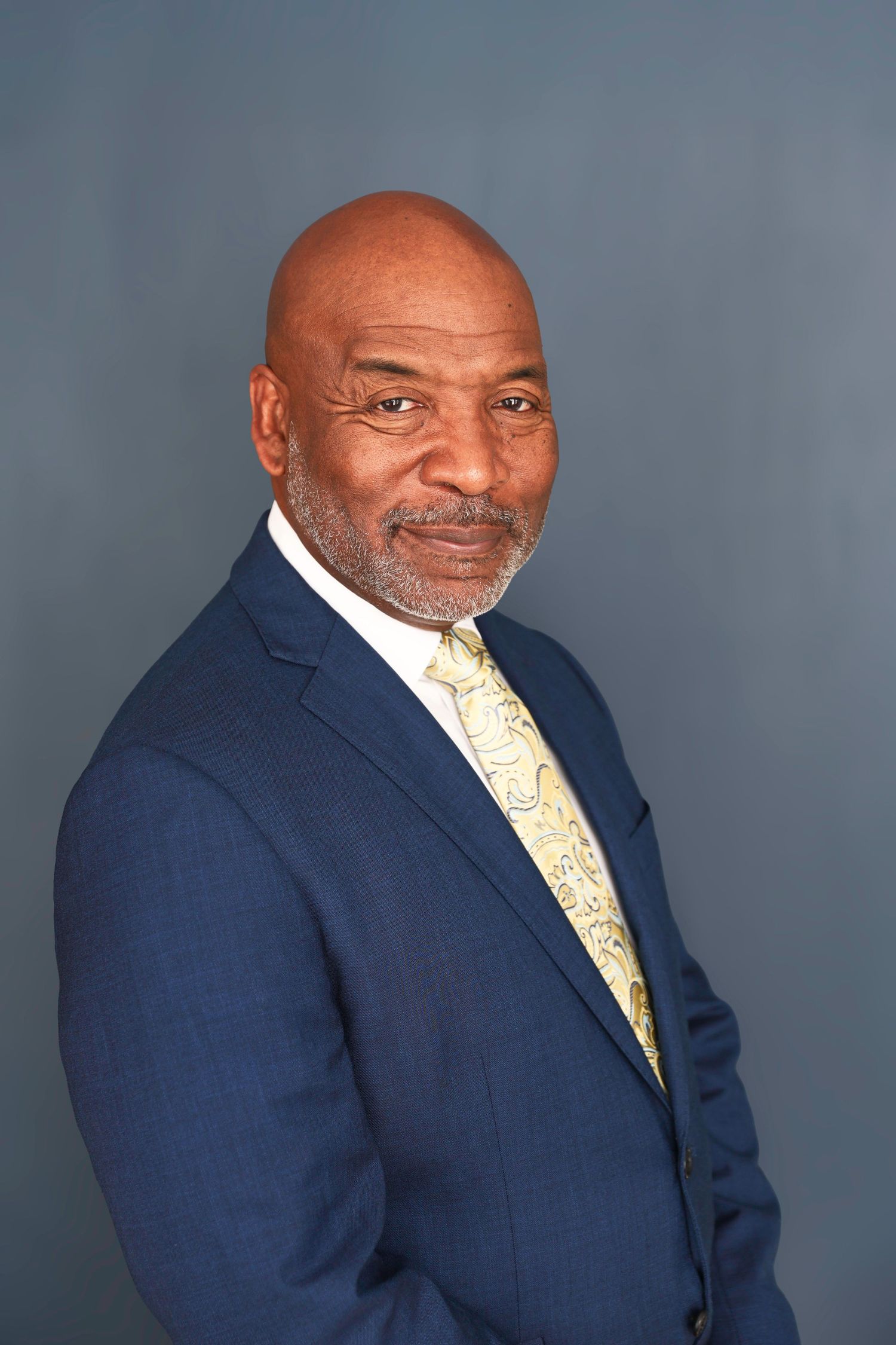 Professional headshot series showing a person in a navy suit and yellow patterned tie against a gray studio backdrop.