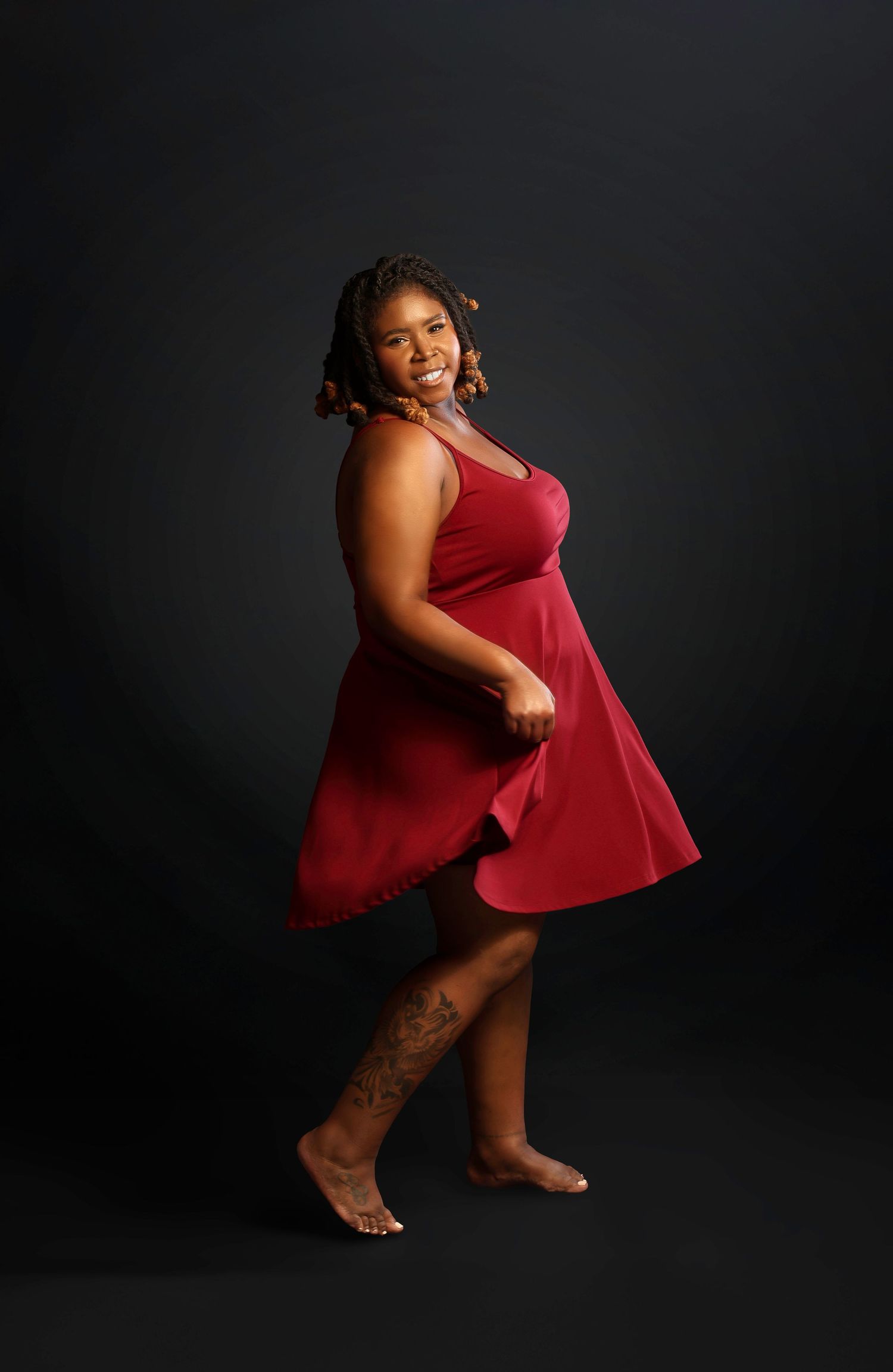 A person in a flowing red dress poses gracefully against a dark background in a studio portrait.