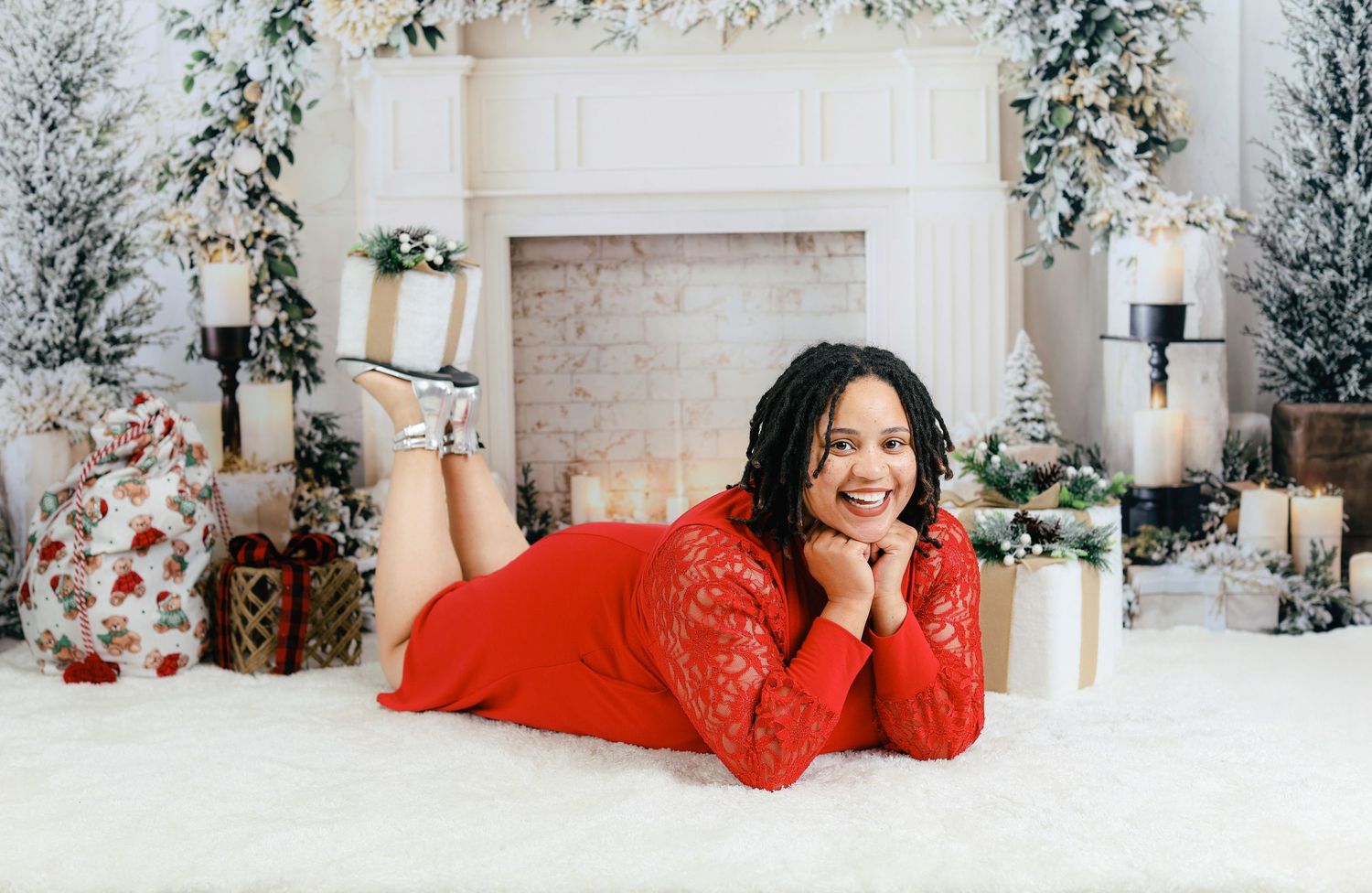 Person in red dress lying on white floor with holiday decorations and greenery in elegant indoor setting.