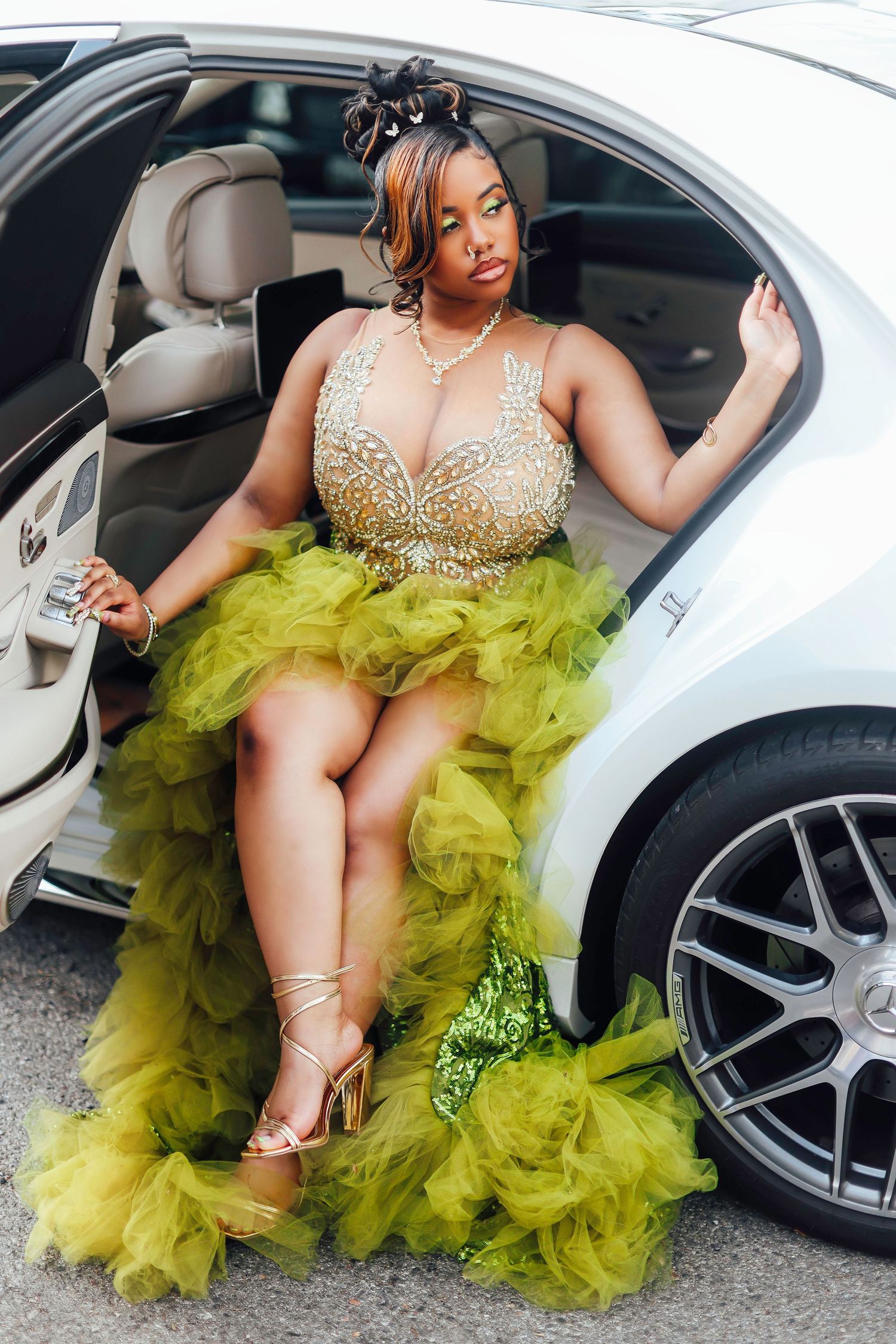 A model in a glamorous chartreuse tulle gown with crystal bodice poses elegantly while stepping out of a luxury car.