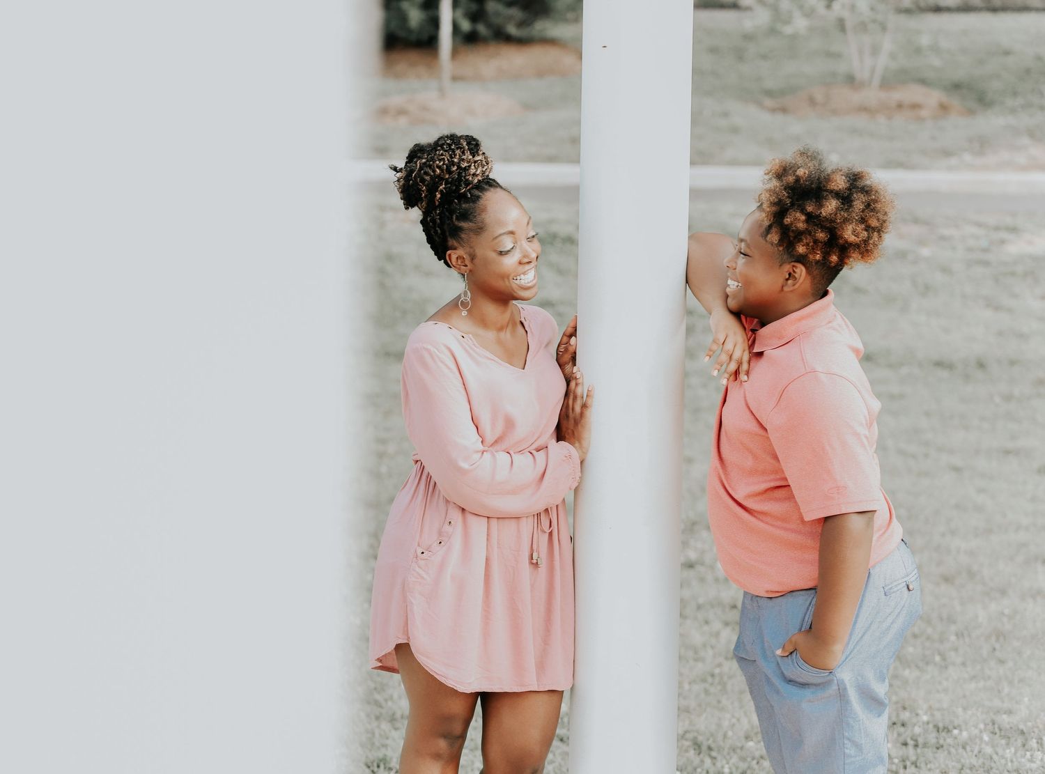 Two people in pink outfits sharing a conversation outdoors next to a white wall.