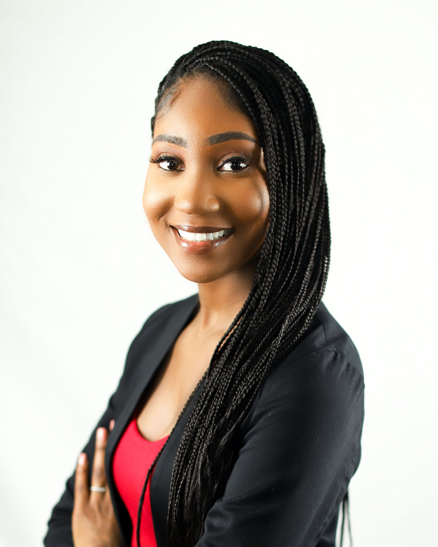 Professional portrait of a person wearing a black blazer and red top against a white background with long braided hair.