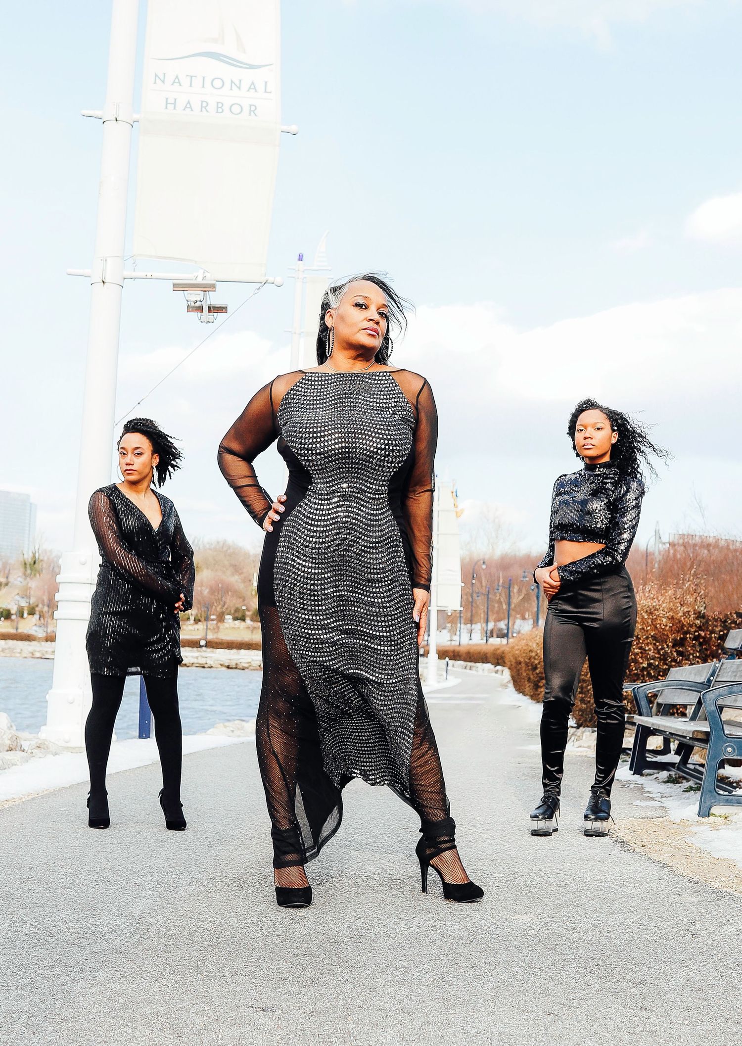 Three people in stylish black outfits posing confidently on an urban waterfront path.