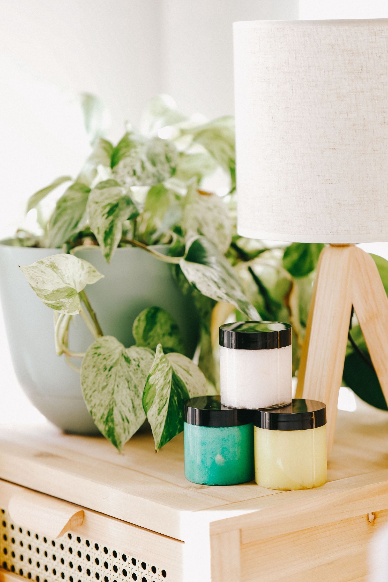 Decorative arrangement of skincare products with a table lamp and potted plant on a wooden surface.